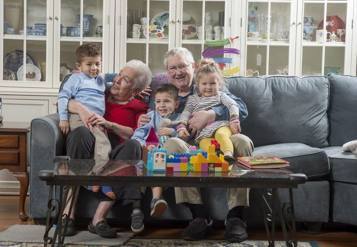 Smiling grandmother and grandfather with three grandchildren, two boys and one girl, seated on sofa