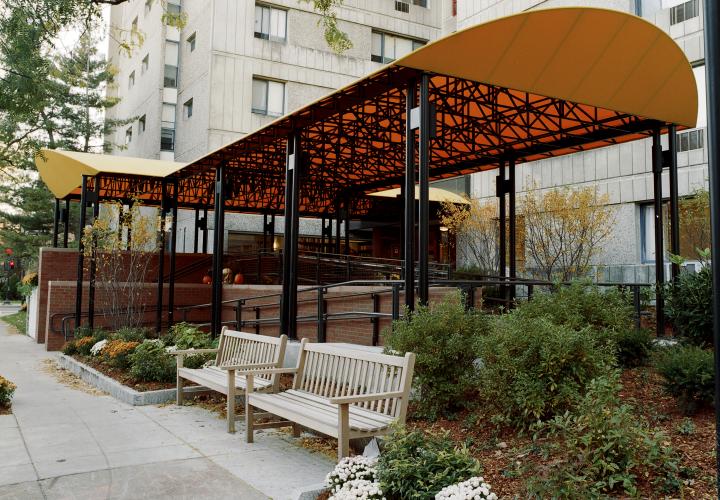 The accessible entrance to 100 Centre Street building of Center Communities of Brookline features green landscaping and a yellow awning.