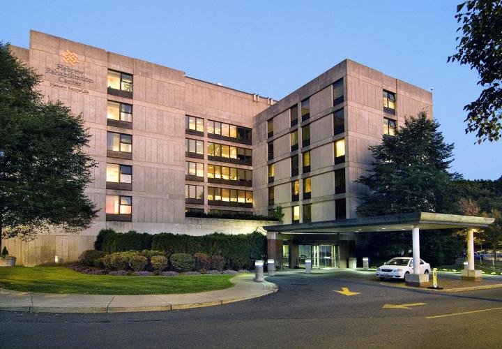 Hebrew Rehabilitation Center at dusk, with white car pulling into horseshoe driveway at entrance.