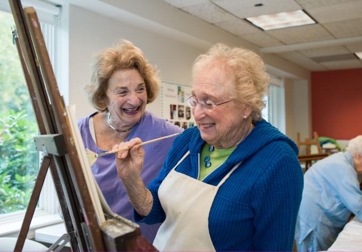 A resident chats with another resident painting on a canvas.