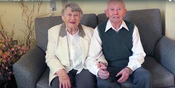 An older couple sitting on a couch, holding hands.