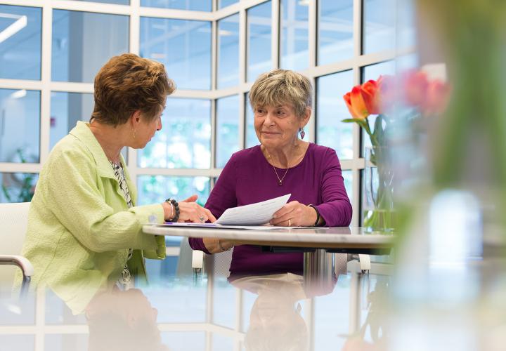 A resident meets with her wellness coach in a sunny lounge overlooking a swimming pool.