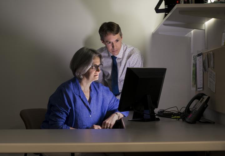 A female senior scientist at the Marcus Institute sits looking at a computer screen while a younger male researcher looks on.