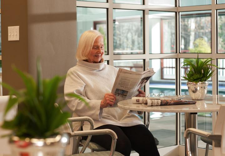 Woman reading newspaper at a table next to the Orchard Cove resident swimming pool