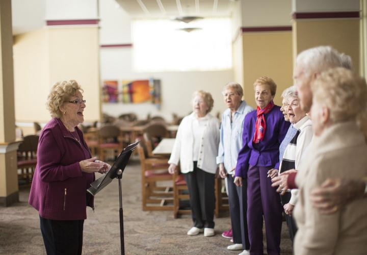 Group of older adults singing in front of a choir director in an open room at Jack Satter House.