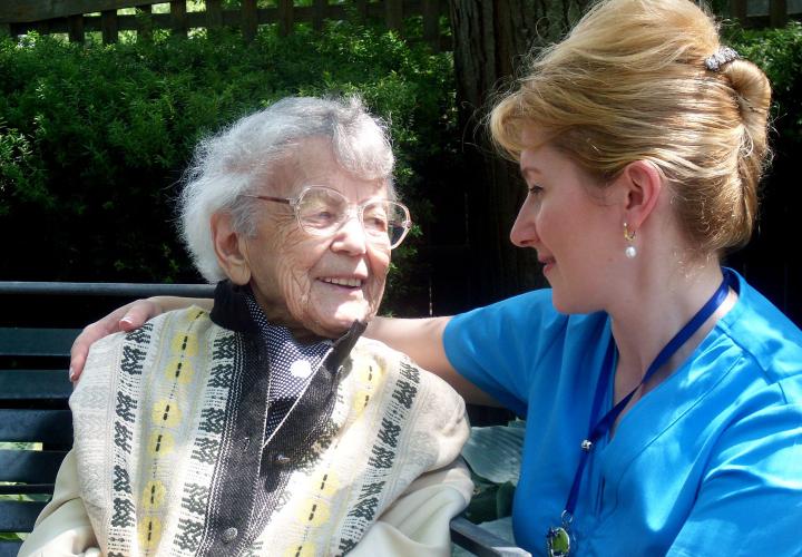 A Hebrew SeniorLife nurse sits with a Russian-speaking senior in an outdoor courtyard at Hebrew Rehabilitation Center in Boston.