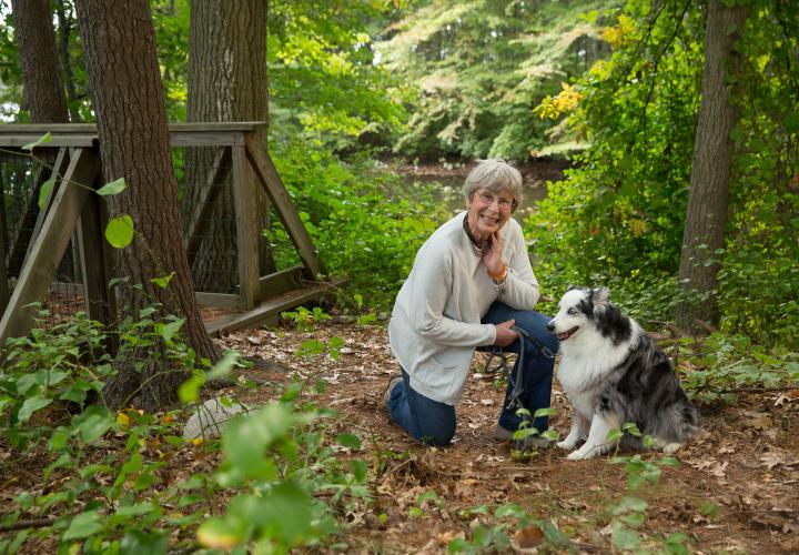 Orchard Cove resident walks her dog along a wooded trail within our 38 acre campus.