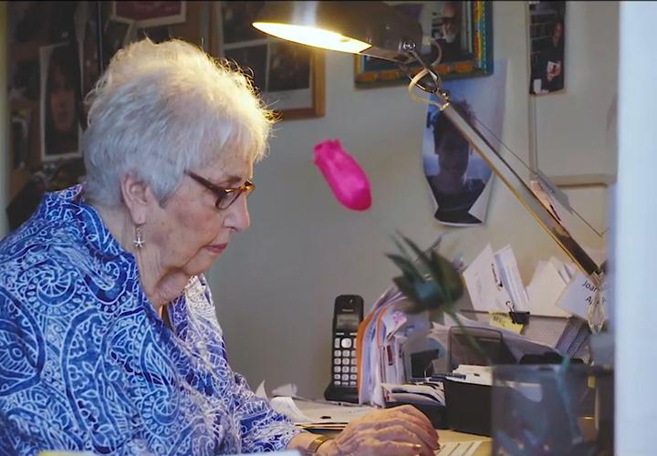 An older woman sits at a desk and types on a keyboard.