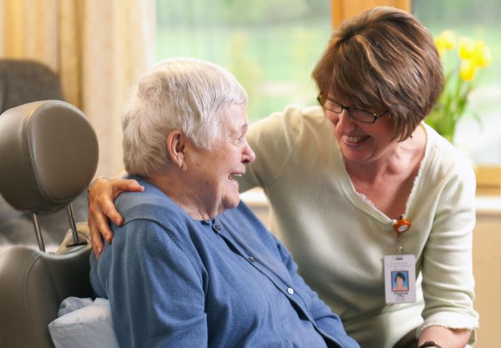 A long-term chronic care patient in a wheelchair smiles at her caregiver.