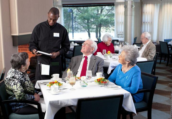 A waiter takes orders from two older women and a man seated at a table in the Pavilion dining room.