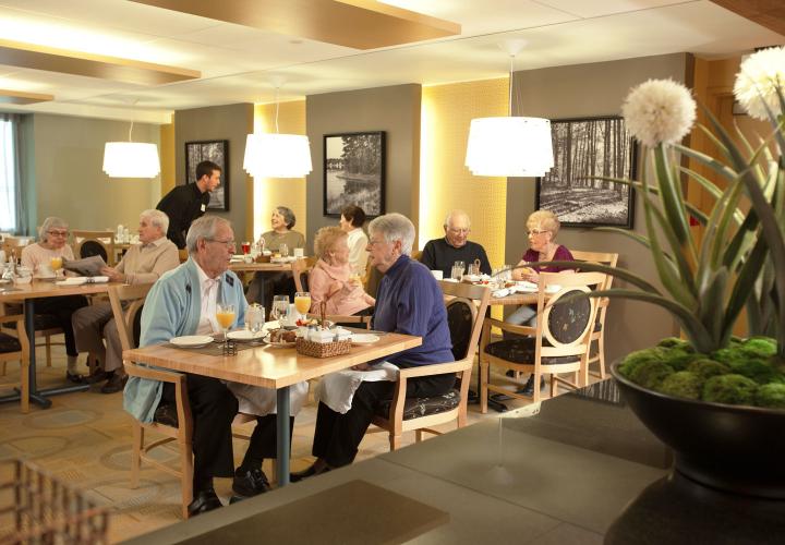 A long shot of older men and women enjoying dining in Orchard Cove’s Pequit dining room.