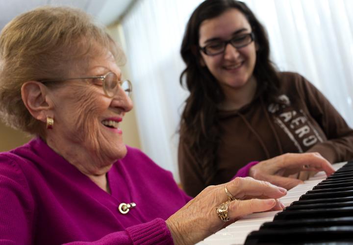 Older woman playing piano with a volunteer.