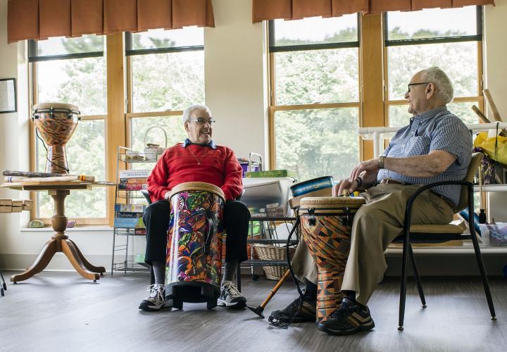 Two residents of memory care assisted living at NewBridge on the Charles enjoy some drumming time in the studio.