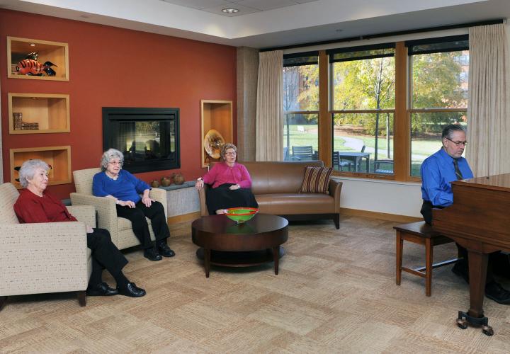 Three residents of assisted living at NewBridge on the Charles listen to an impromptu jazz piano concert in our “living room” common space.