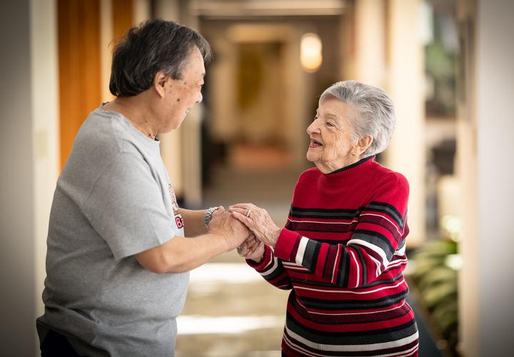 A man and woman stand in a hallway at the Simon C. Fireman Community, facing each other and holding hands as they talk.