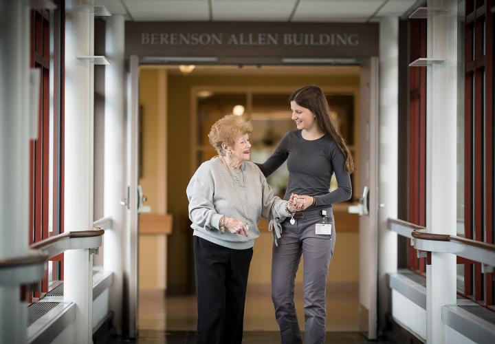 A student walks with a senior in a glass halfway at Hebrew Rehabilitation Center in Boston. Hebrew SeniorLife offers internships and clinical training opportunities for students looking to work with older adults.