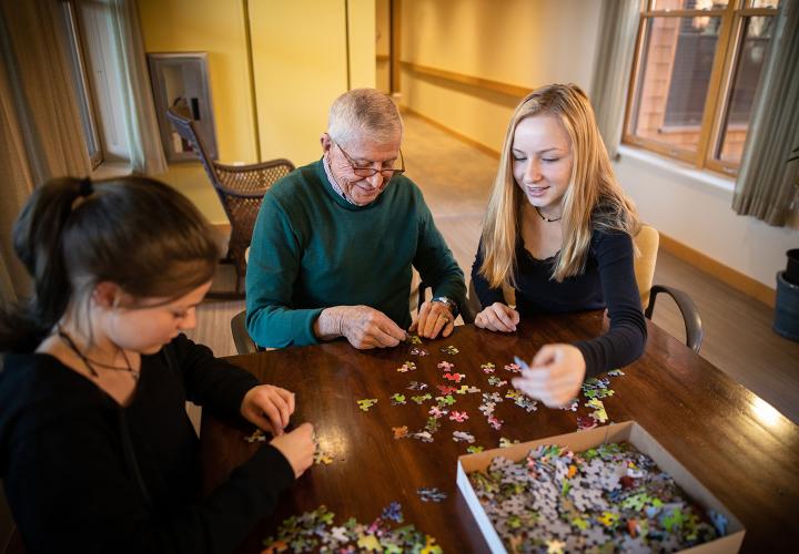 An older gentleman works on a puzzle with two young girls.