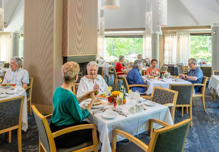 Older men and women seated at multiple tables enjoying meals at The Pavillion dining room