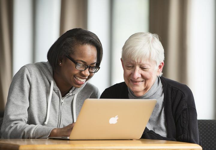 Younger woman and older woman sitting together in front of a computer smiling.