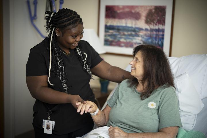 A certified nurse assistant holds the hand of a female patient while talking to her.