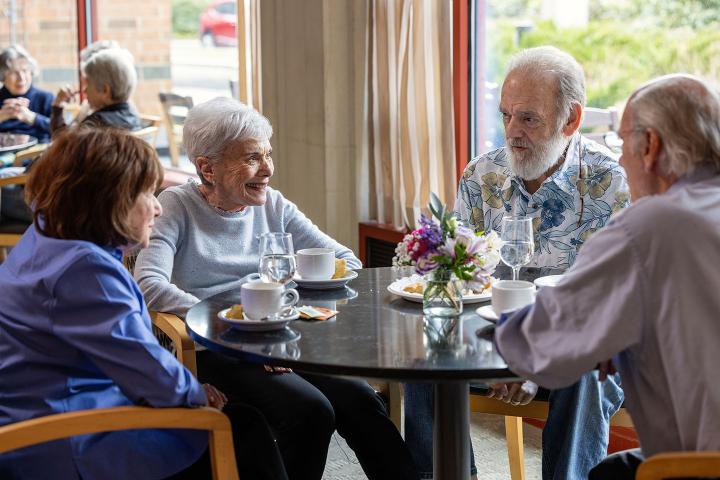Four seniors enjoy a lively conversation around a table.