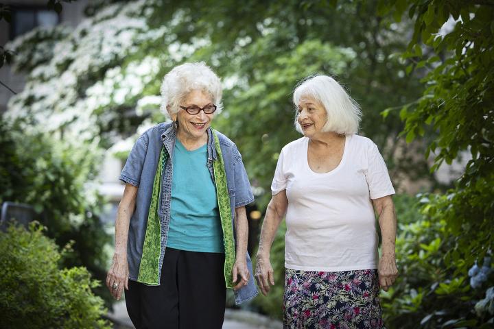 Two older women talk while walking down a garden path.