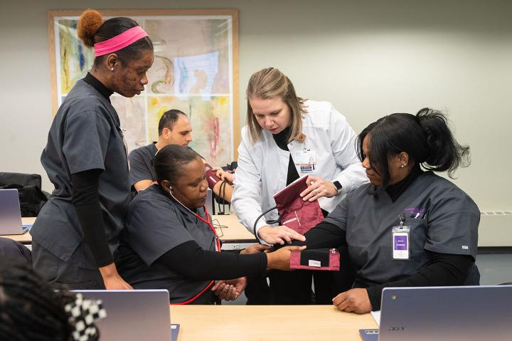 An instructor shows nursing trainees how to use a blood pressure cuff.