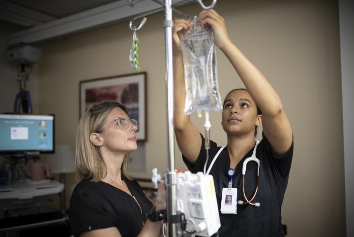 A nurse manager supervises as a nurse changes an IV bag.