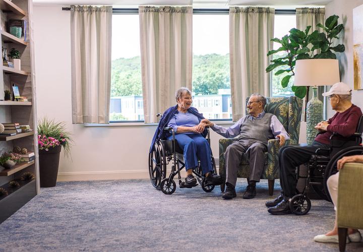 An older couple holding hands while enjoying a sunny seating area.