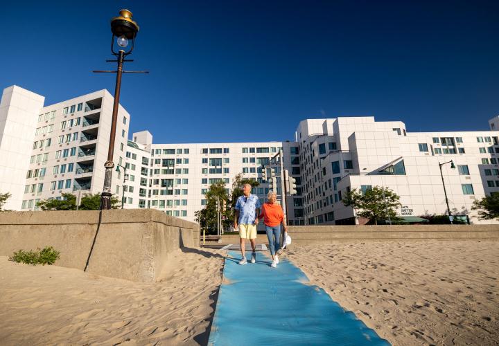 An older couples walks up the beach toward the Jack Satter House.
