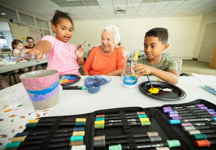 An older female resident paints with two young children.