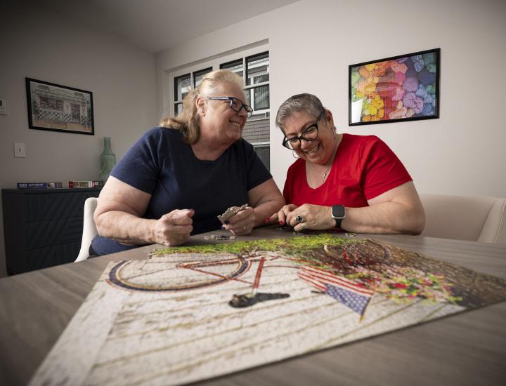 Two older women laugh together while doing a puzzle.