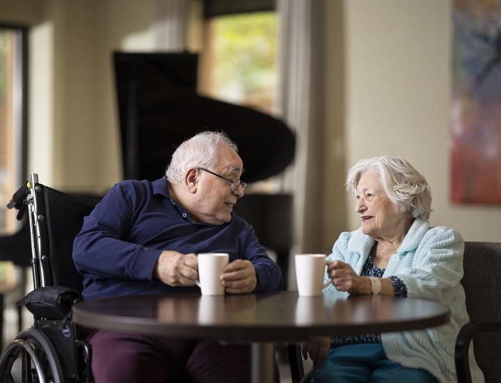 An older male patient and an older female patient having a conversation at a table.