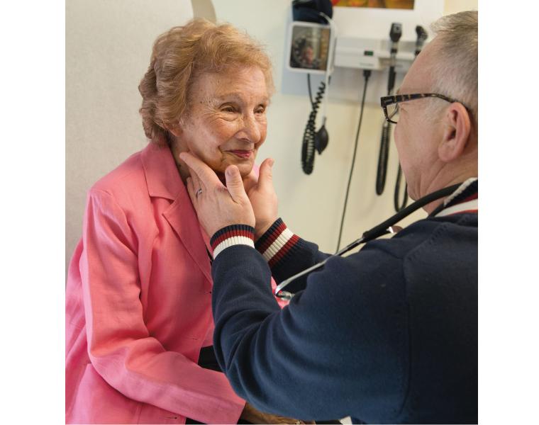 Older adult in pink sweater interacts with a doctor during a visit.