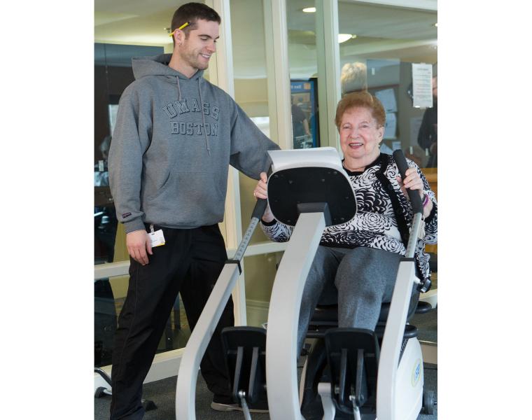 A resident uses specialized fitness equipment for seniors as an exercise instructor looks on.
