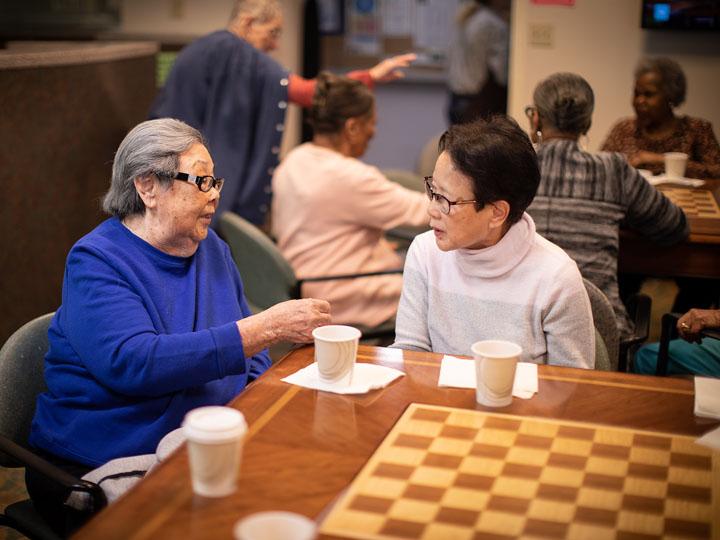 Two older women sit drinking coffee at the coffee shop at Simon C. Fireman Community in Randolph, MA.