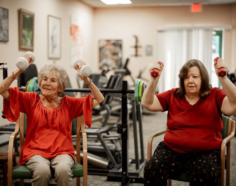 Two older women lift hand weights in a fitness room.