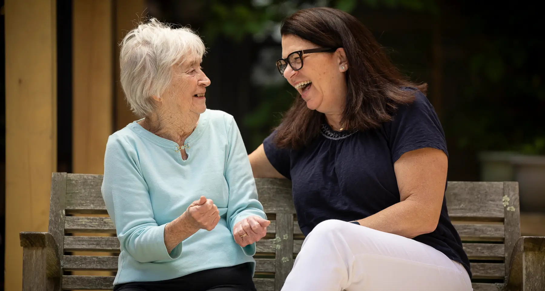 two women of different ages sharing a laugh on a park bench