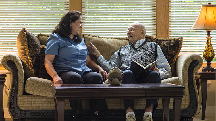 a father and his adult daughter laugh together on a sofa